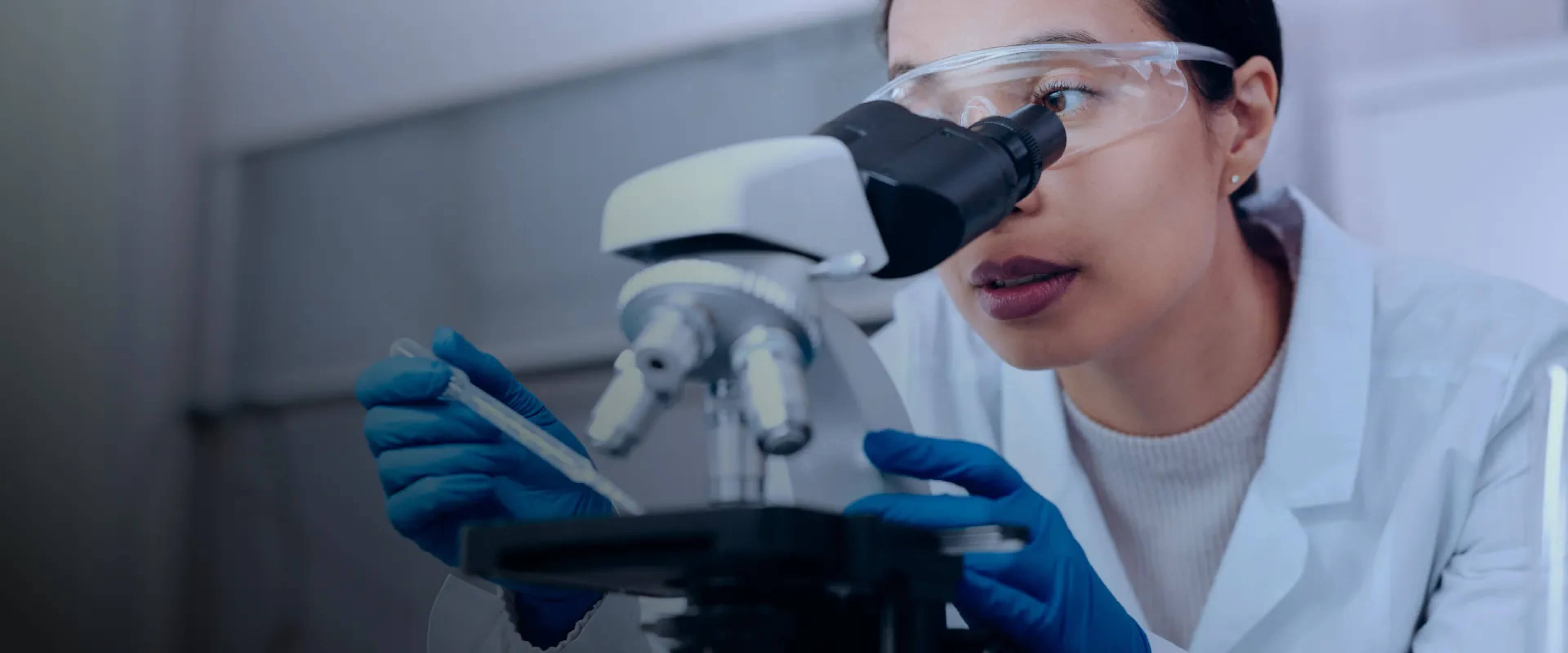 Chercheuse en blouse blanche utilisant un microscope en laboratoire