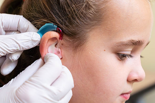 A close-up of a child receiving a hearing aid fitting in their ear by a healthcare professional.
