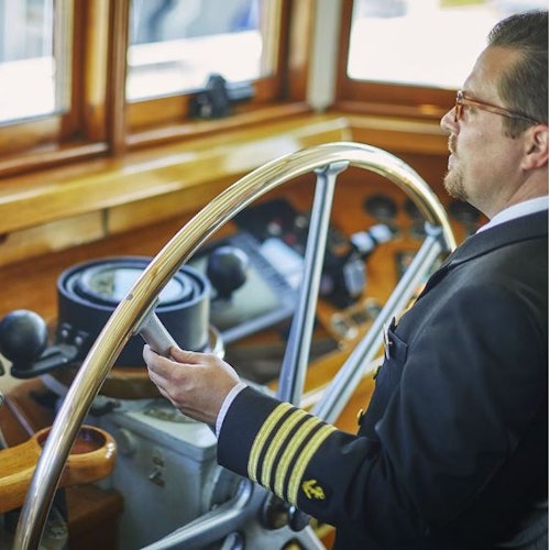 一位穿着船长制服的男子在船桥内使用大型轮盘驾驶船只。