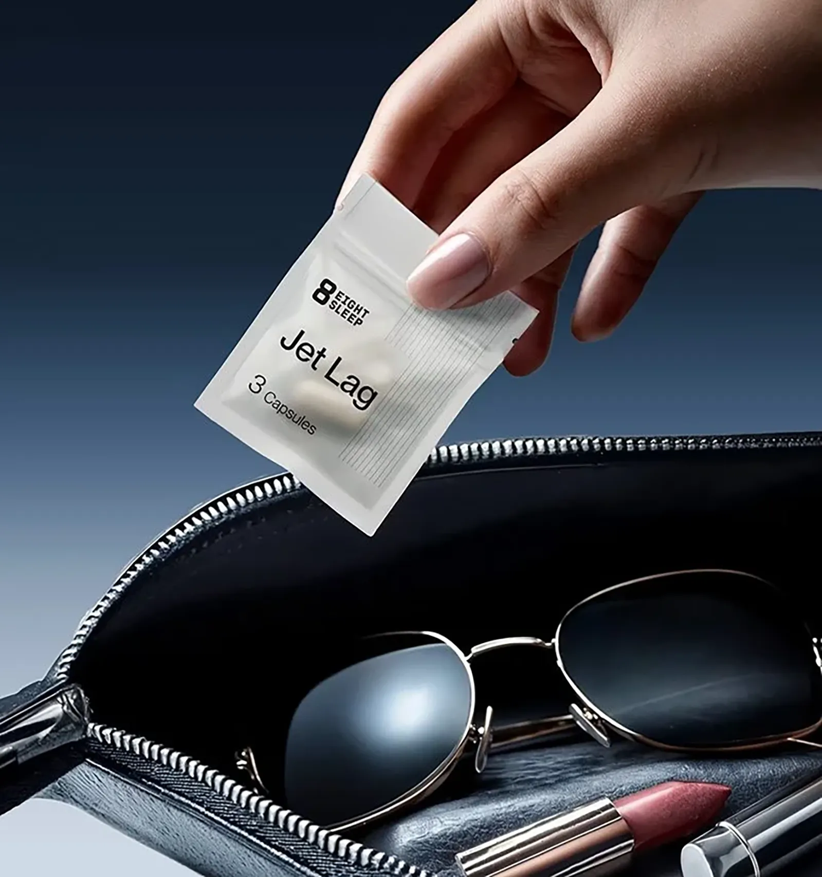Hand placing an Eight Sleep Jet Lag supplement sachet into an open travel bag