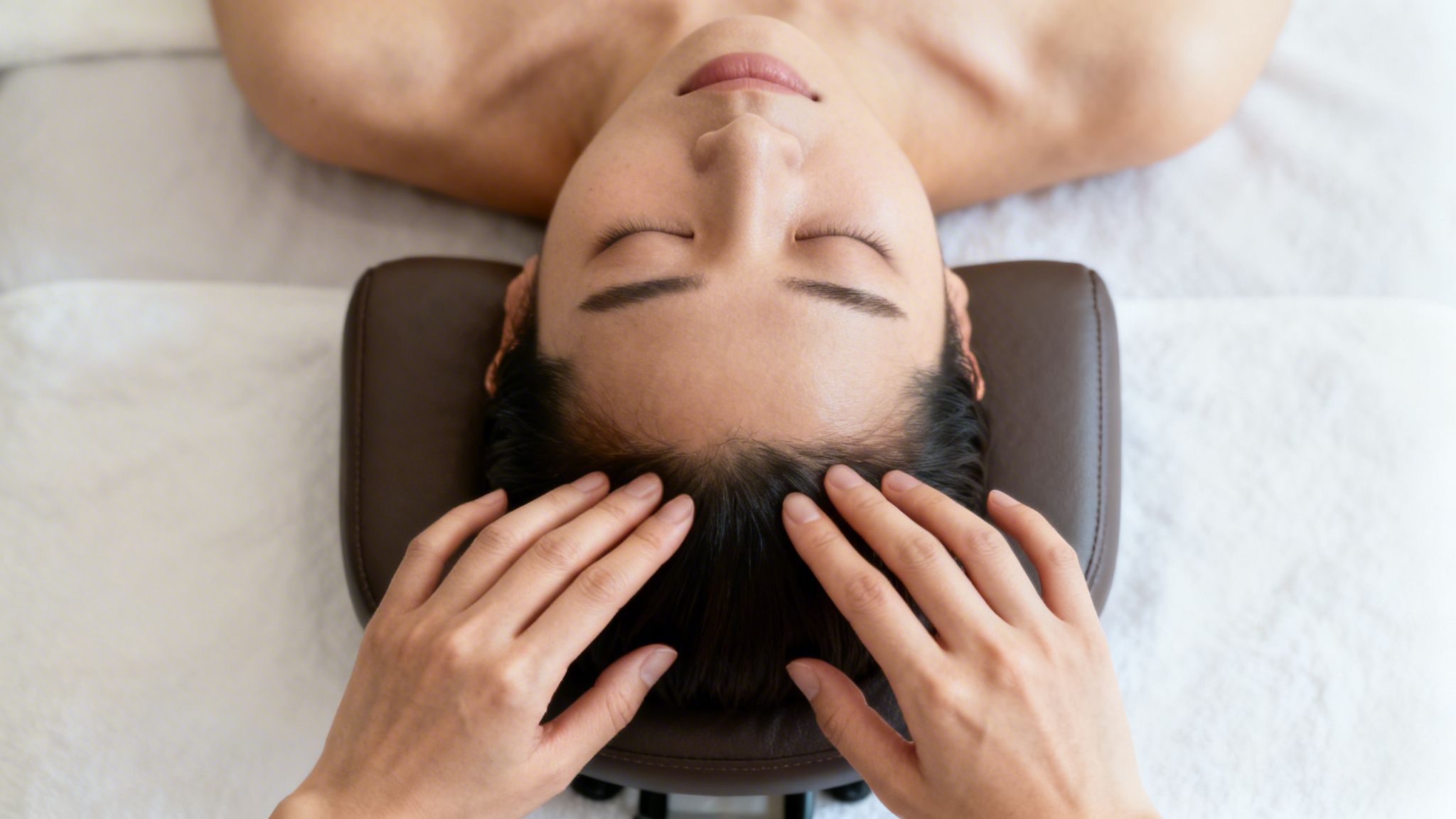 A person with closed eyes receiving a relaxing scalp massage on a treatment bed.