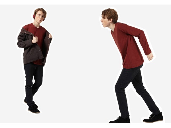Two young men are shown against a plain light gray background. The man on the left wears a dark gray/brown jacket over a red shirt and black pants, with black shoes and over-ear headphones. His right arm is bent at the elbow, and his left arm is slightly extended. The man on the right wears a maroon long-sleeved shirt and black pants, with black shoes. His right arm is extended forward, and his left arm is bent at the elbow. Both are looking toward the right side of the frame.