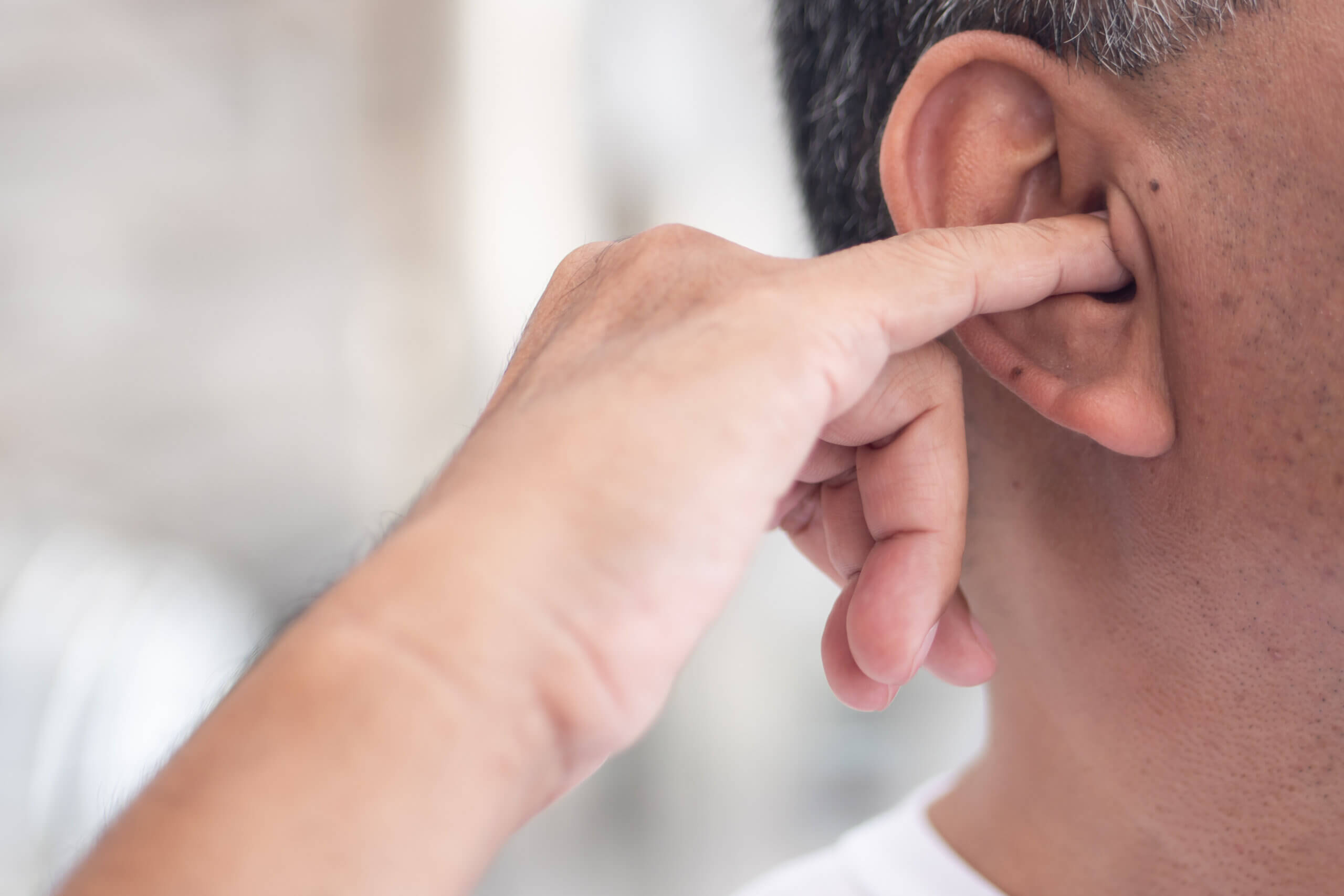 A close-up of a hand gently touching someone's ear, with a soft background.