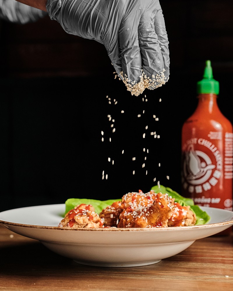 Fotografia kulinarna przedstawiająca rękę posypującą sezamem danie w stylu azjatyckim
