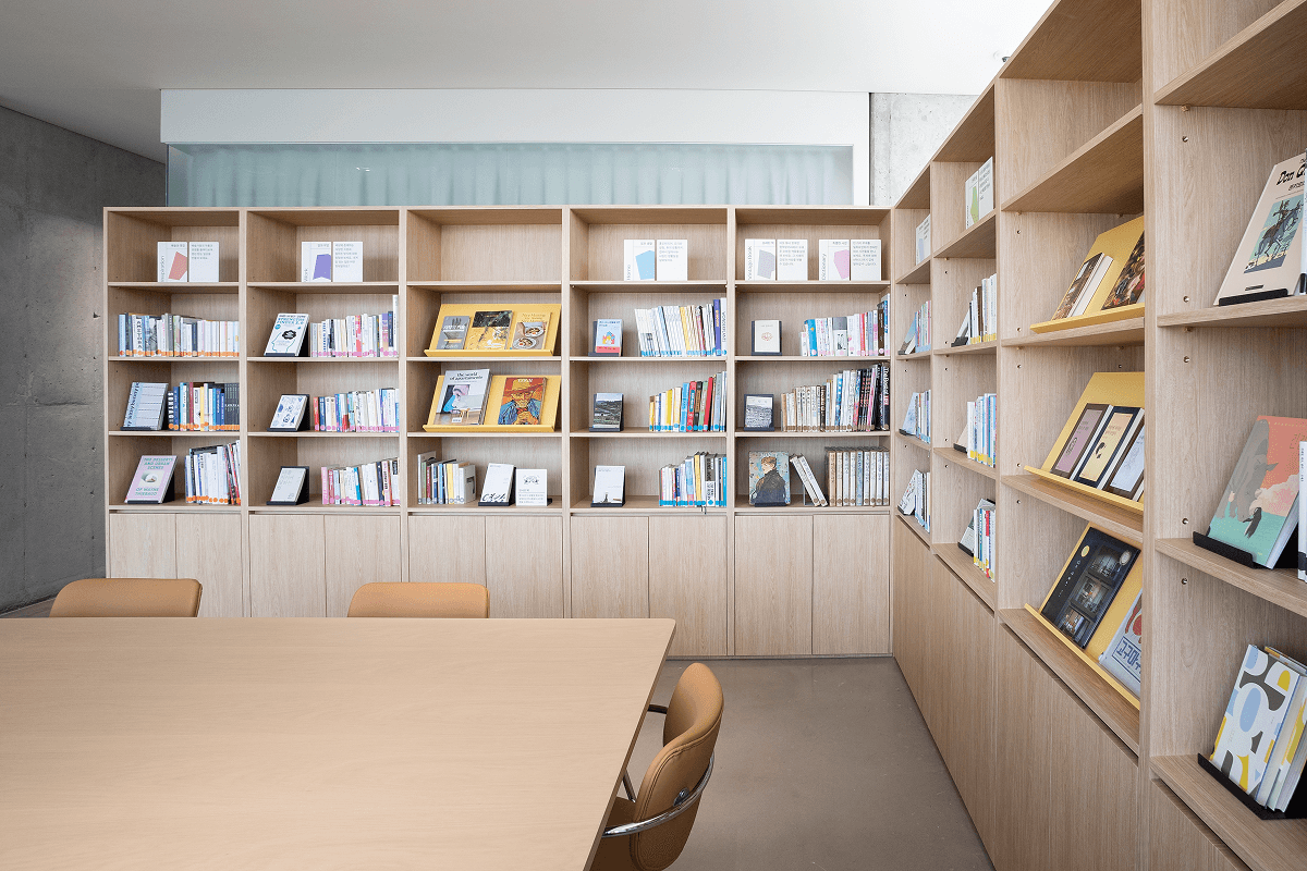 Library on the 20th floor of Mangrove Sinseol with curated bookshelves on both sides of a large lounge table.