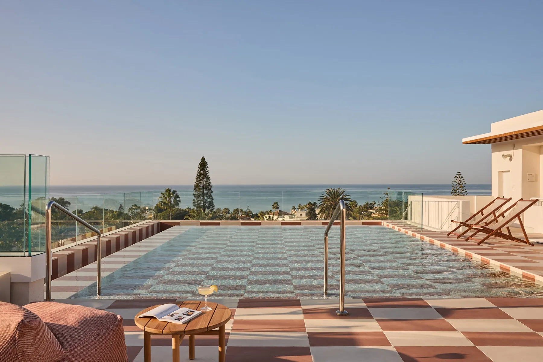 Ein Rooftop-Pool mit Blick auf das Meer, Liegestühle, ein Tisch und ein Cocktail.