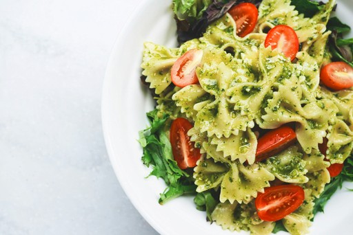 A plate of pasta with pesto, cherry tomatoes, and greens, garnished and served on a white dish.