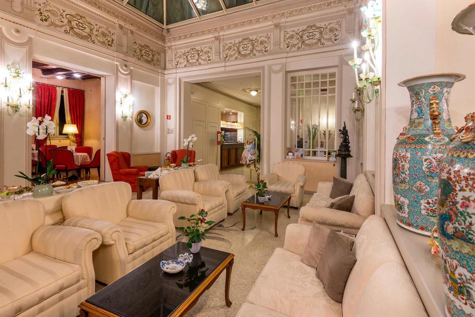 A luxurious hotel lobby with plush cream armchairs, a large patterned vase, and ornate white architectural moldings.