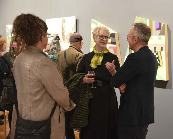 Art gallery visitors engaging in conversation, discussing abstract paintings on display.