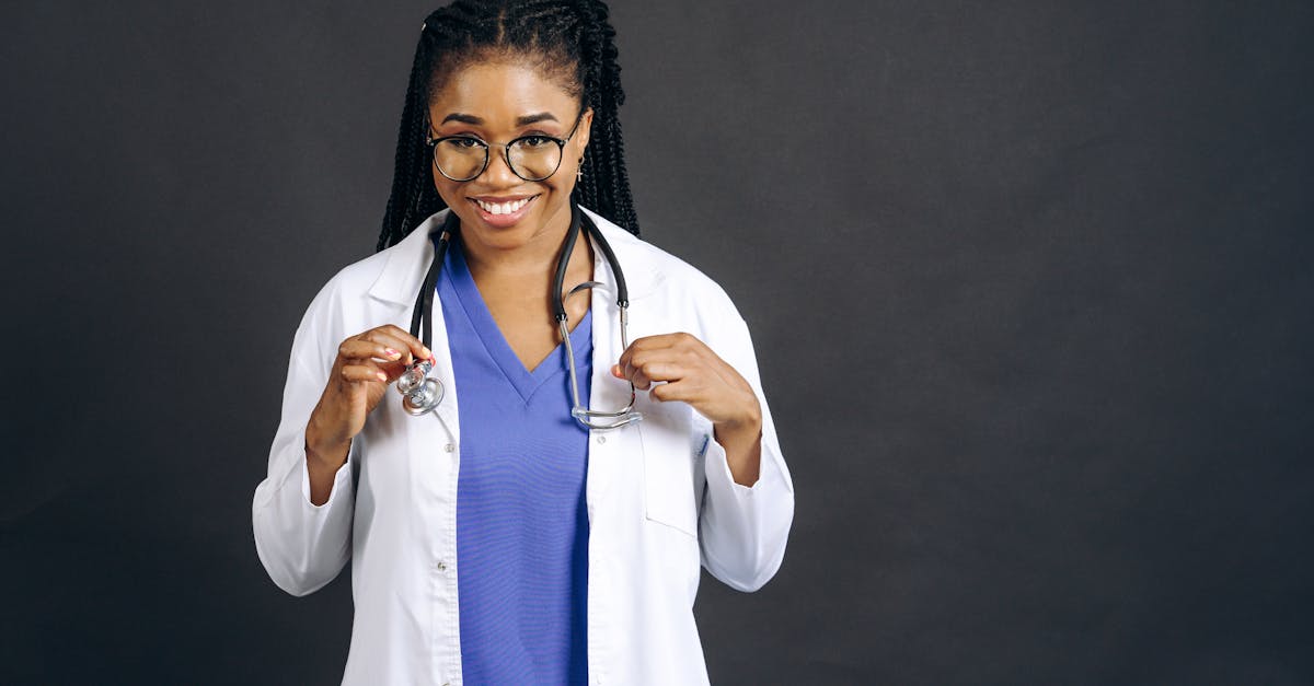 Portrait of a smiling female doctor wearing eyeglasses and a lab coat against a gray background.