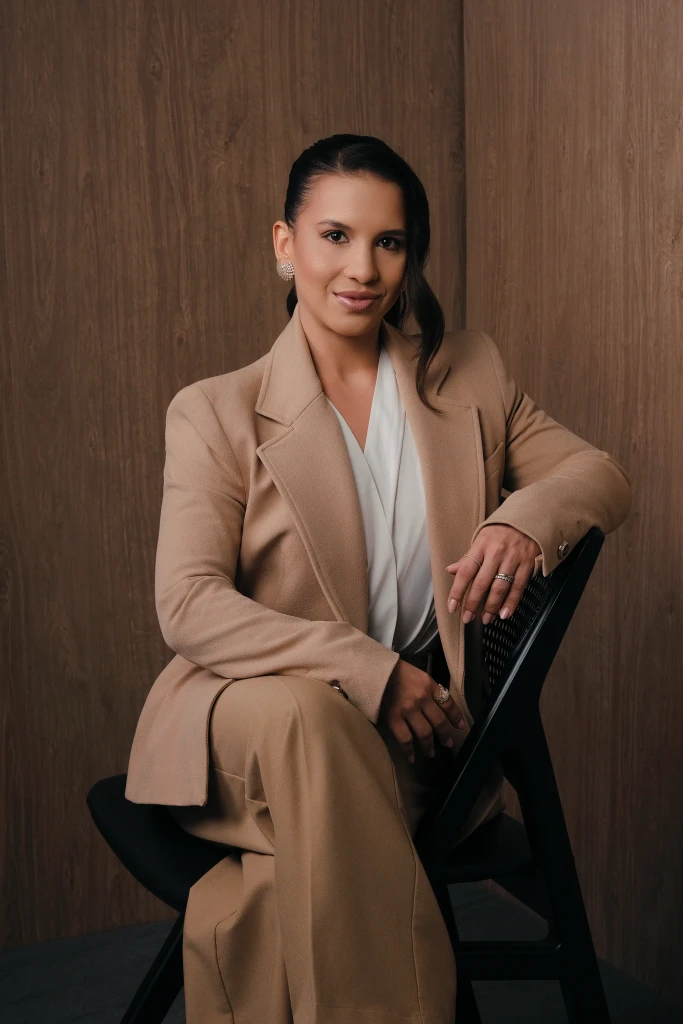 Isabela Ramos com blazer bege e calça social sentada em cadeira – foto profissional corporativa