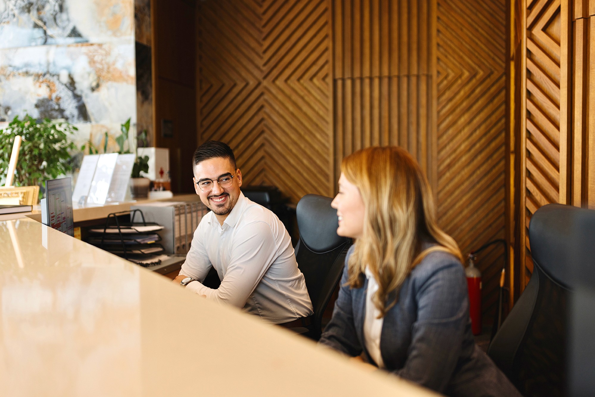 Two people working behind a hotel receiption smiling at each other