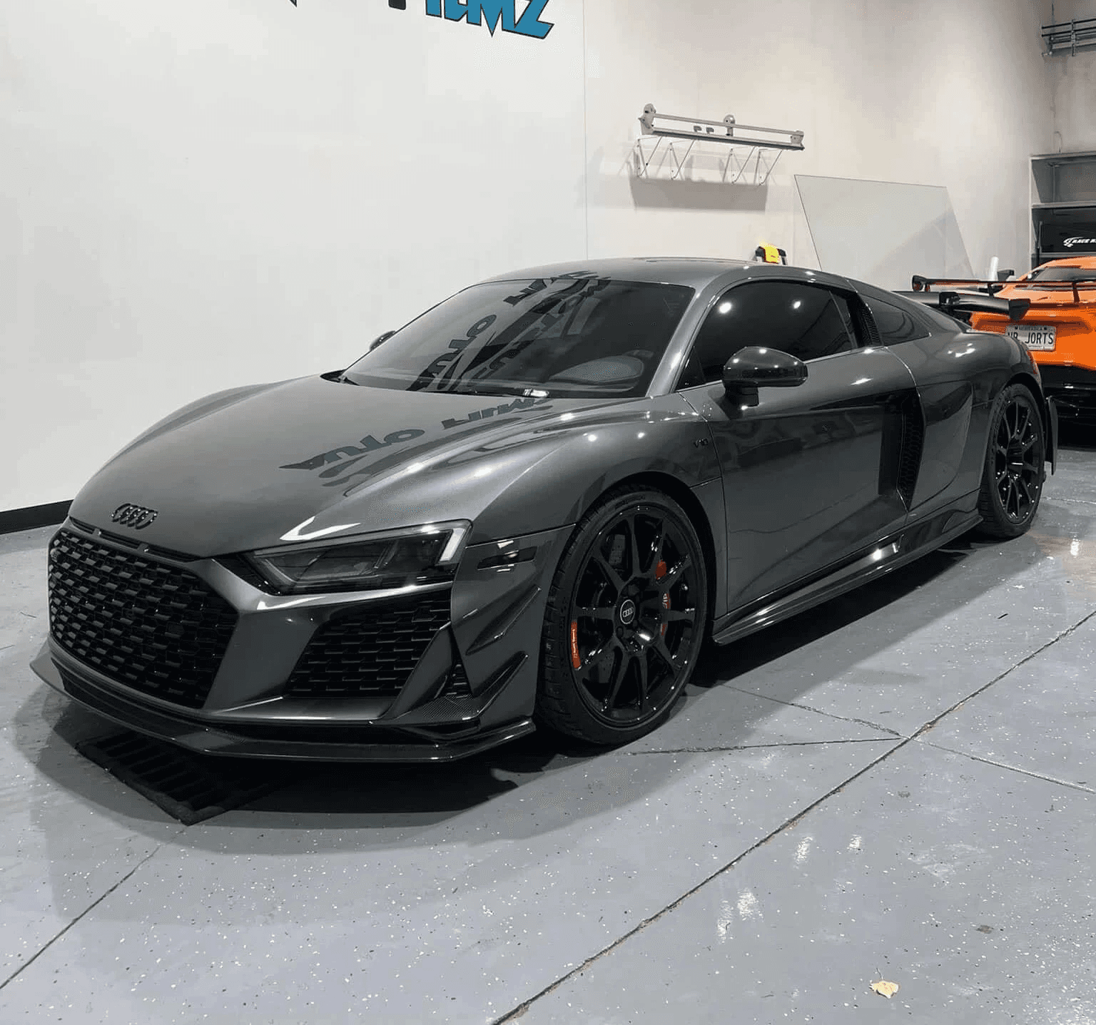 A sleek gray Audi R8 sports car is parked indoors on a polished concrete floor.