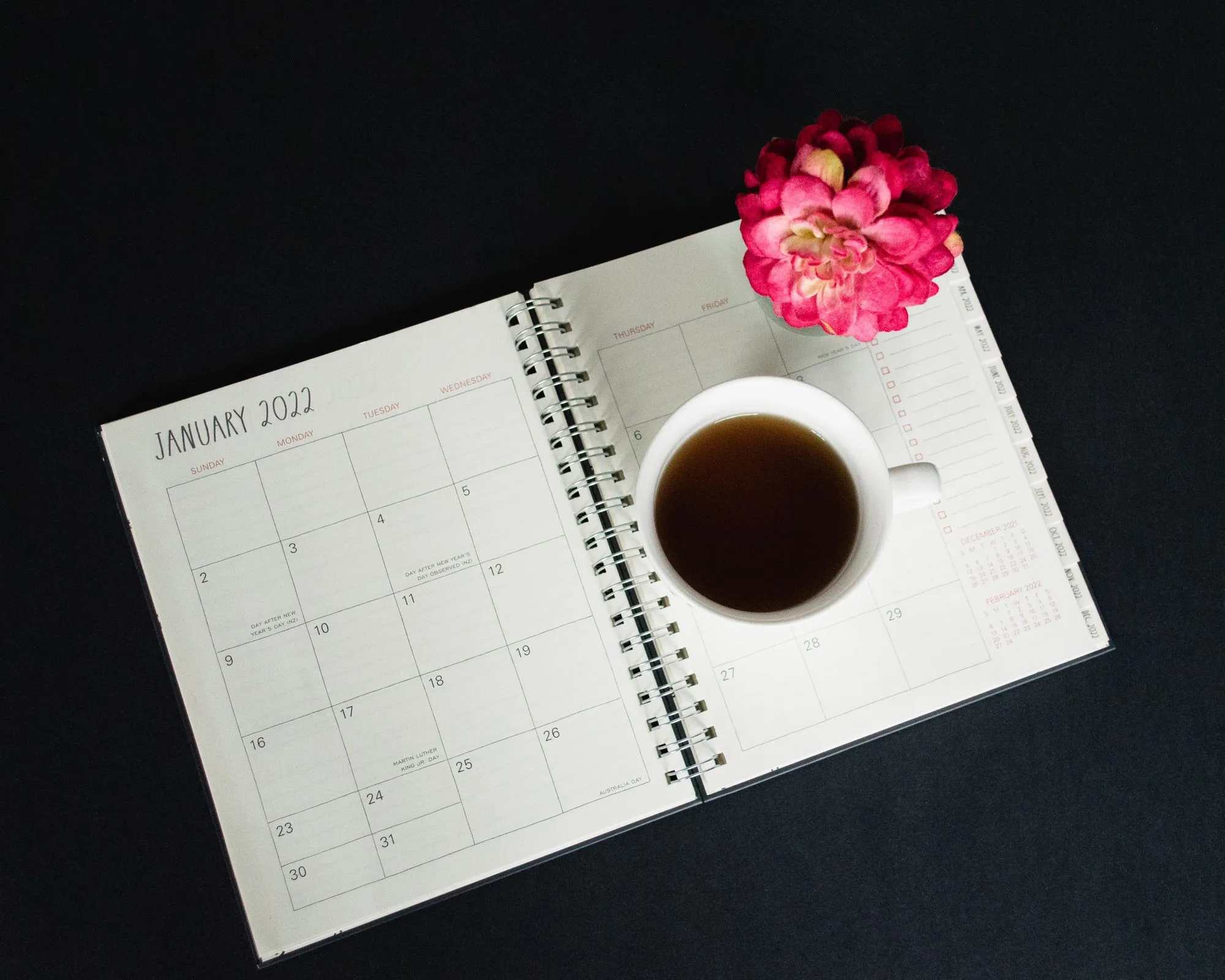 Photo of a calendar book opened to January 2022, with a cup of coffee and fuchsia-colored flower on one page