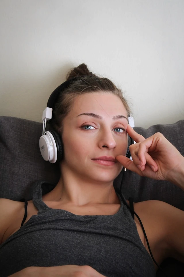 Woman wearing over-ear headphones resting on a couch with a thoughtful expression.