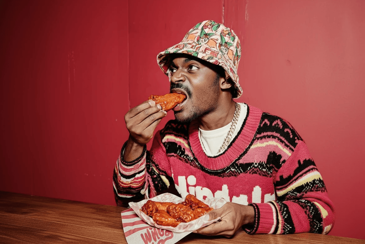 Lifestyle-Portrait beim Genuss von Buffalo Wings mit buntem Bucket-Hat für authentische Food-Kampagne