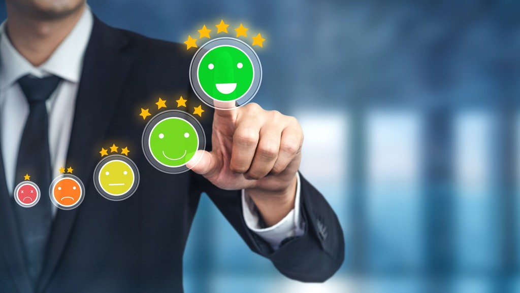 Executivo selecionando avaliação máxima em escala de satisfação com emojis de vermelho a verde com estrelas, representando métricas de experiência do cliente e qualidade em TI - FindUP - Customer Success