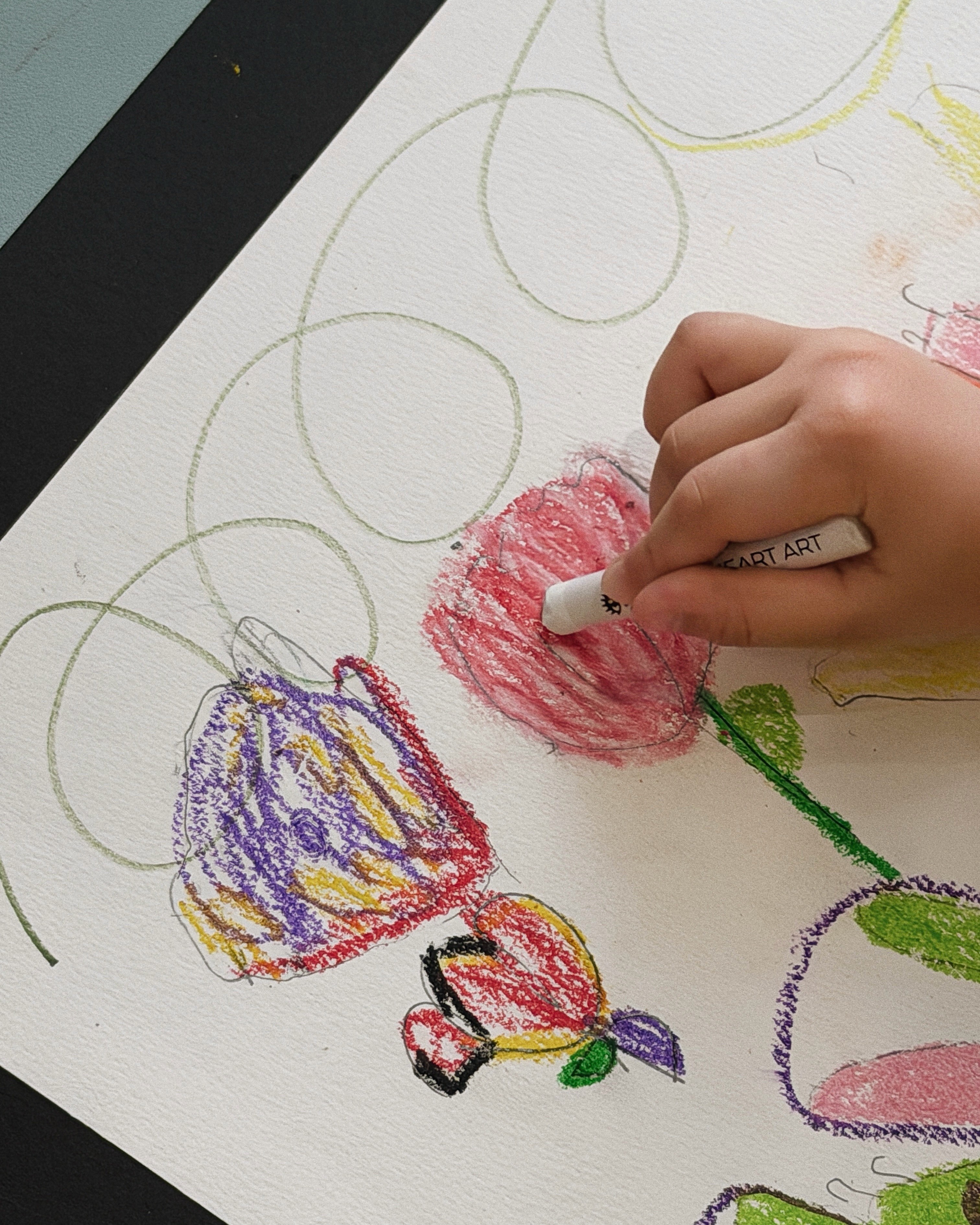 A child placing their hands on a sketchpad, surrounding them with colorful crayon drawings of flowers and creatures in a Noljak summer art class at Rookids BGC.