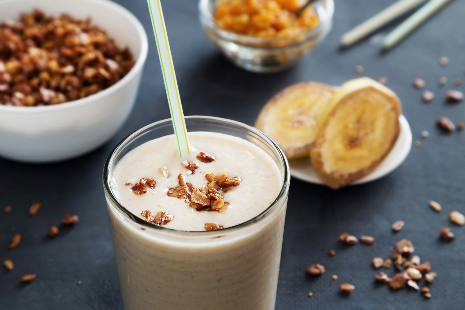 A creamy blended smoothie topped with granola in a glass, beside slices of banana — an easy way to drink extra calories.