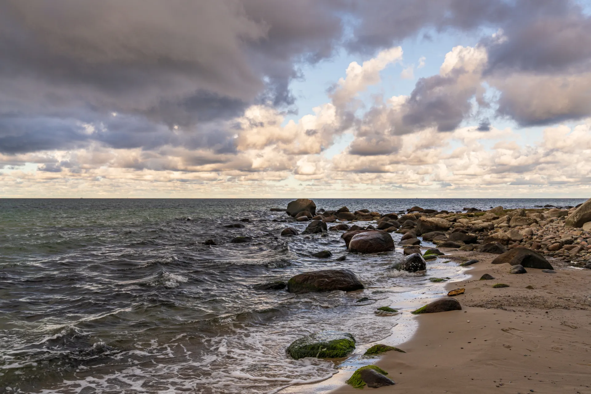 Ein Strand in Mecklenburg-Vorpommern. An der Küste sind mehrere kleine Steine und die Wellen schlagen auf diese ein.