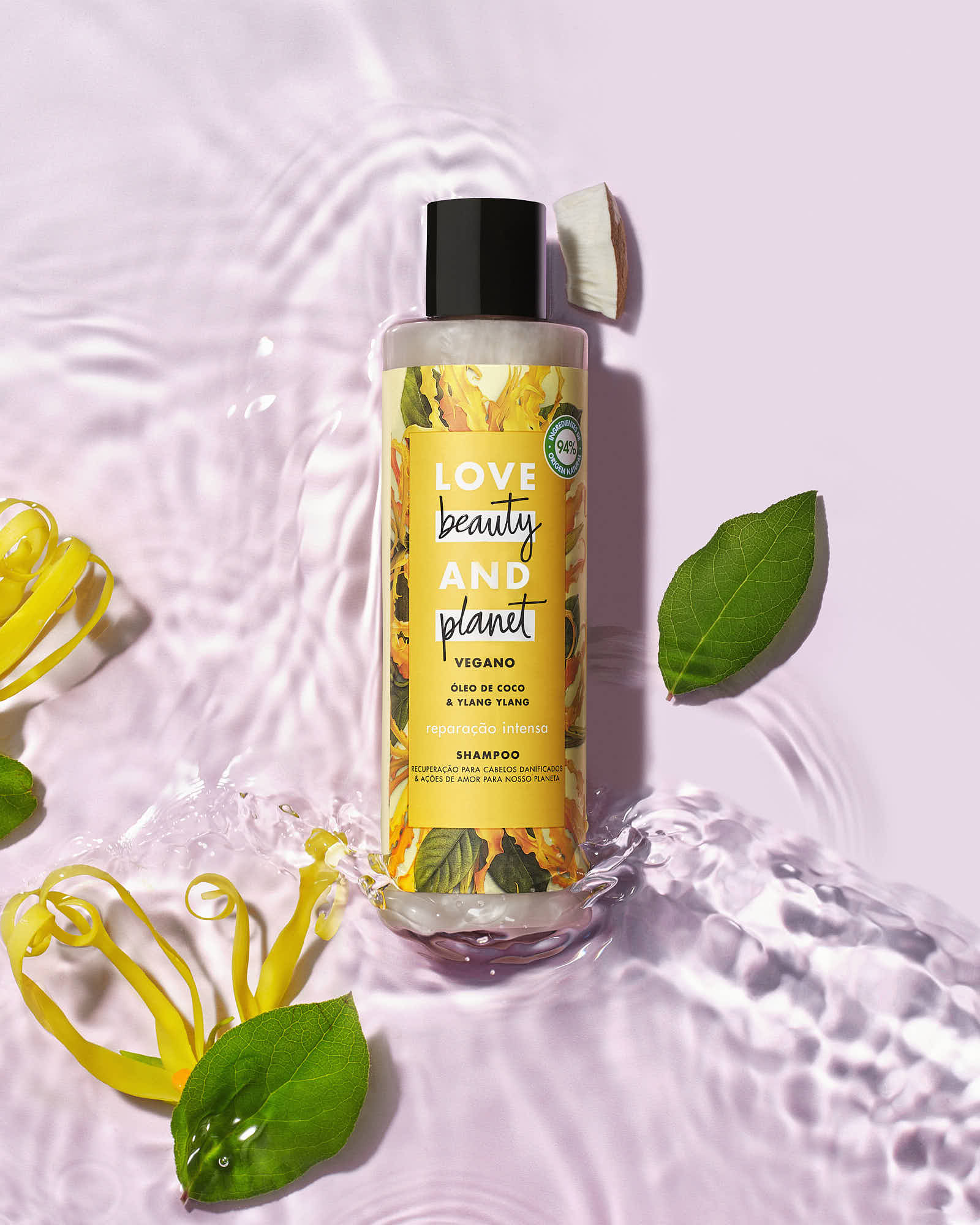 A yellow bottle of product rests on a light pink surface, surrounded by leaves and flower petals.