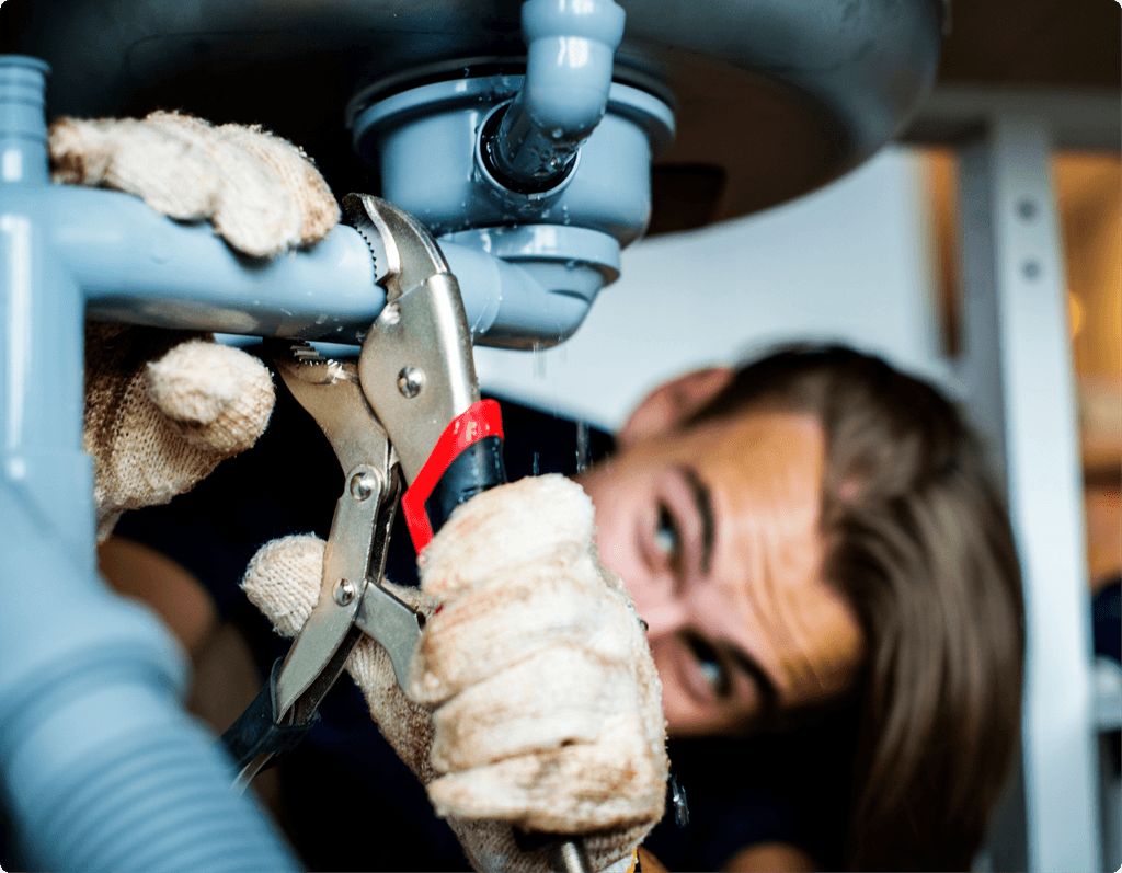 Plumber fixing pipes under a sink with a wrench. Wearing gloves, focused on repairing the plumbing.