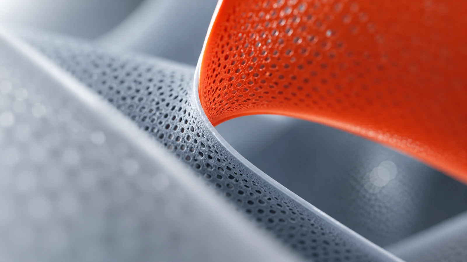 Perforated grey surface curving beneath an orange perforated sheet