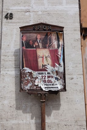 A photo of a poster, put on a pedestal and on top of it the word SPQR which is the name of the Roman empire.