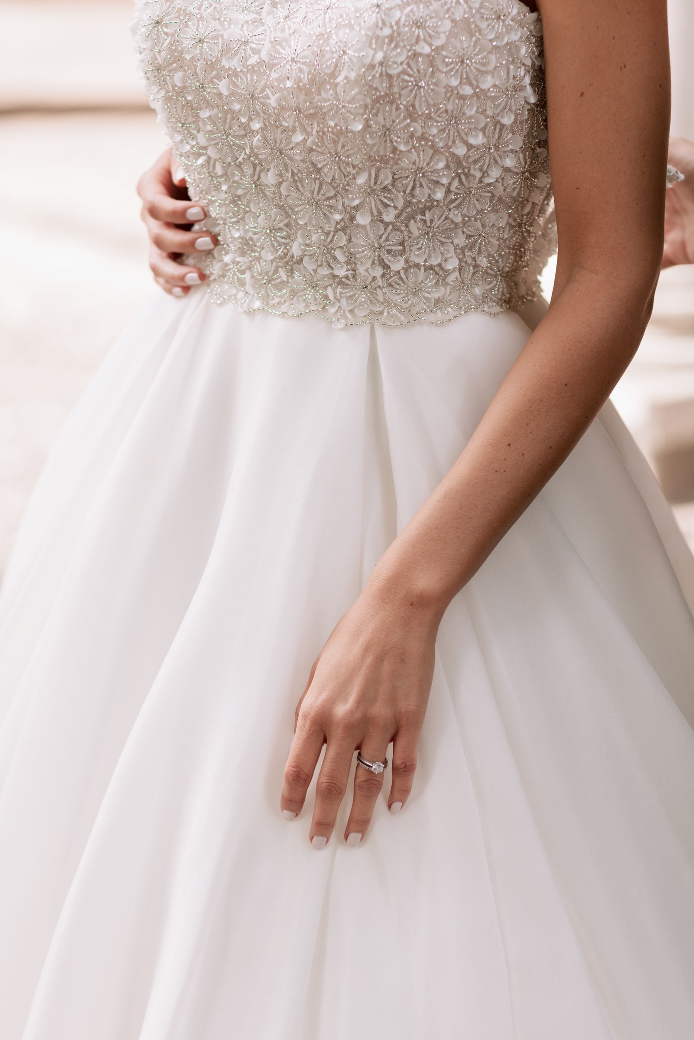 Sposa in abito bianco con corpetto ricamato, anello nuziale in primo piano, a Villa Ferrari