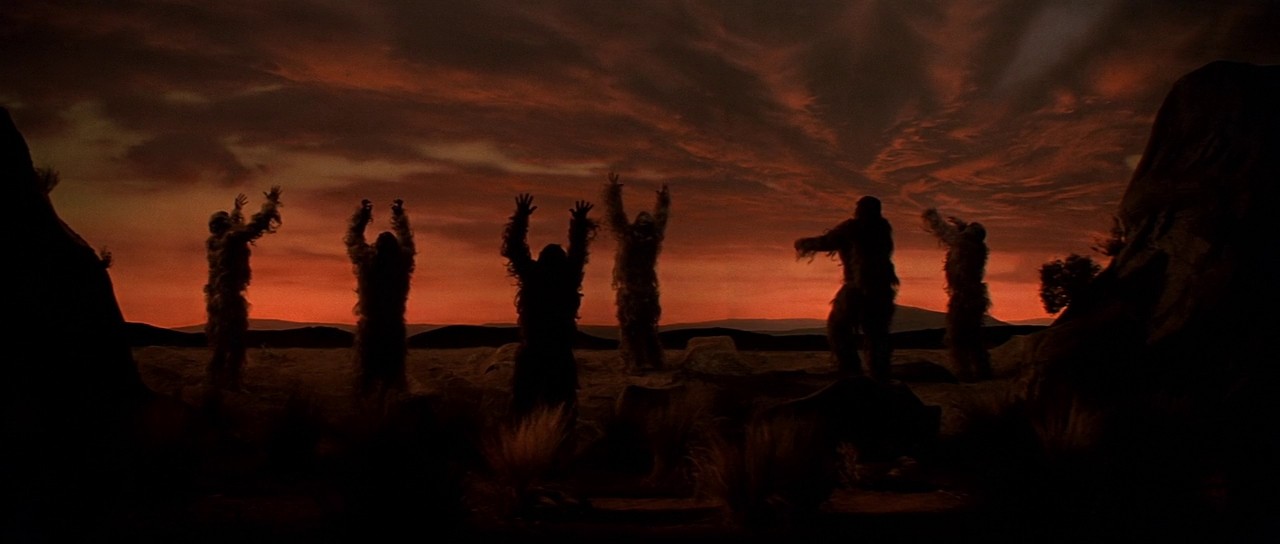 Two fathers carrying children on shoulders on a mountain path.