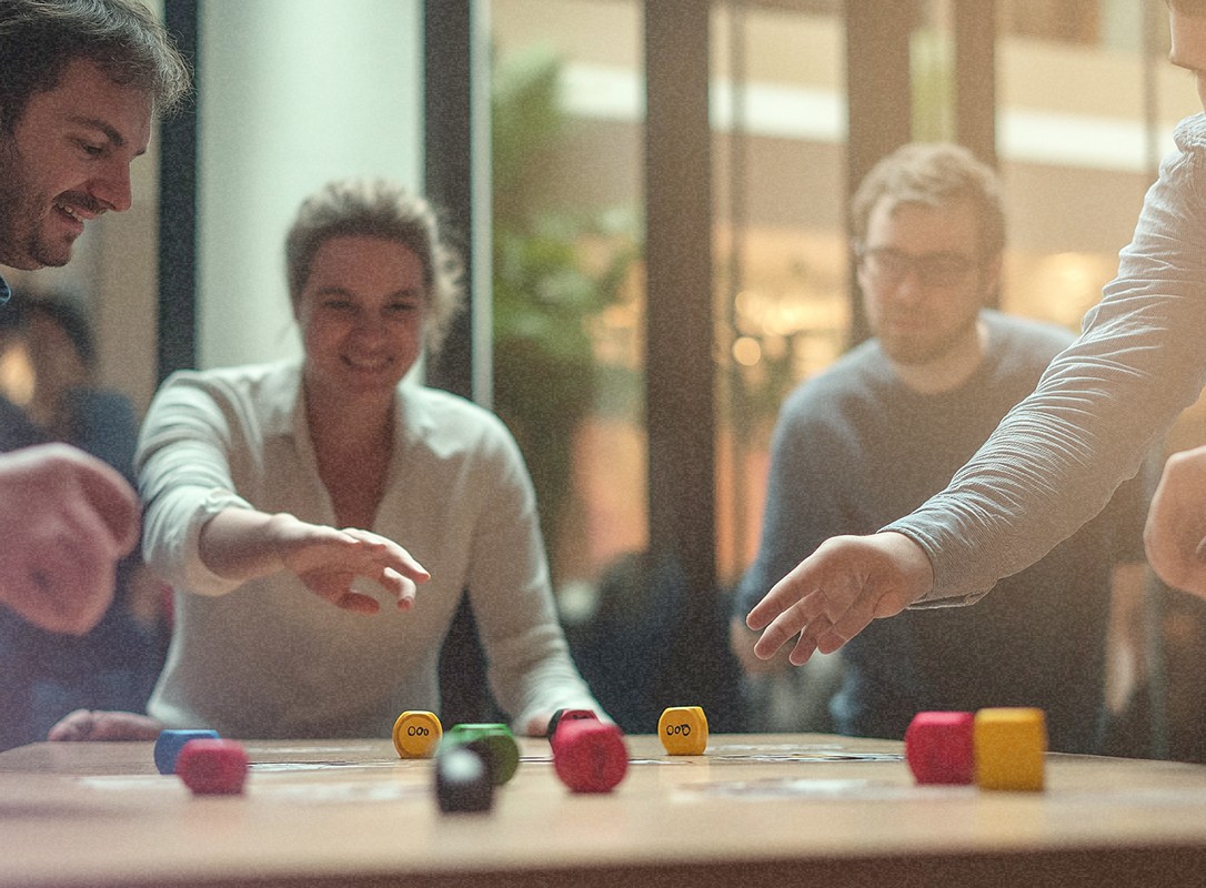 Groupe de personnes jouant à un jeu avec plusieurs cubes de couleurs (rouge, vert, jaune) qui sont disposés sur la table.