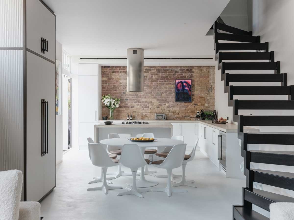 A contemporary London kitchen renovation designed by residential architects, featuring an exposed brick splashback wall, sleek white cabinetry, a modern concrete island, and an integrated gas stovetop.