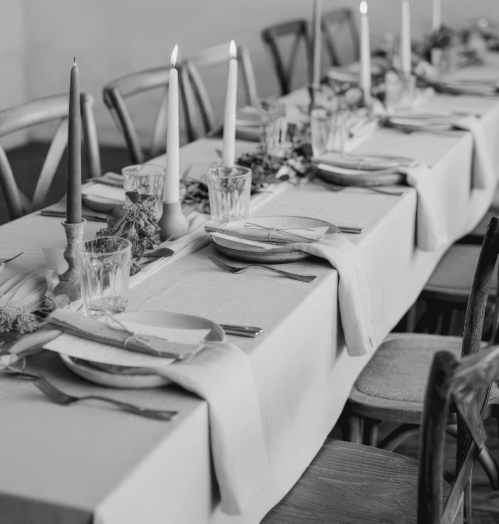 A beautifully set dining table with white tablecloth, cutlery, and fresh greenery in a cozy, well-lit space.
