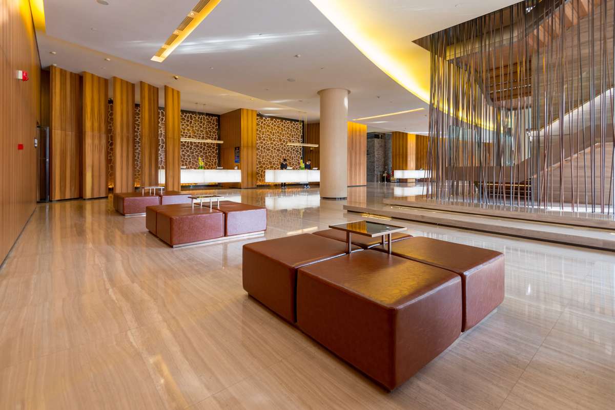 Modern hotel lobby with tan leather modular seating, a polished stone floor, and a decorative metal mesh wall.