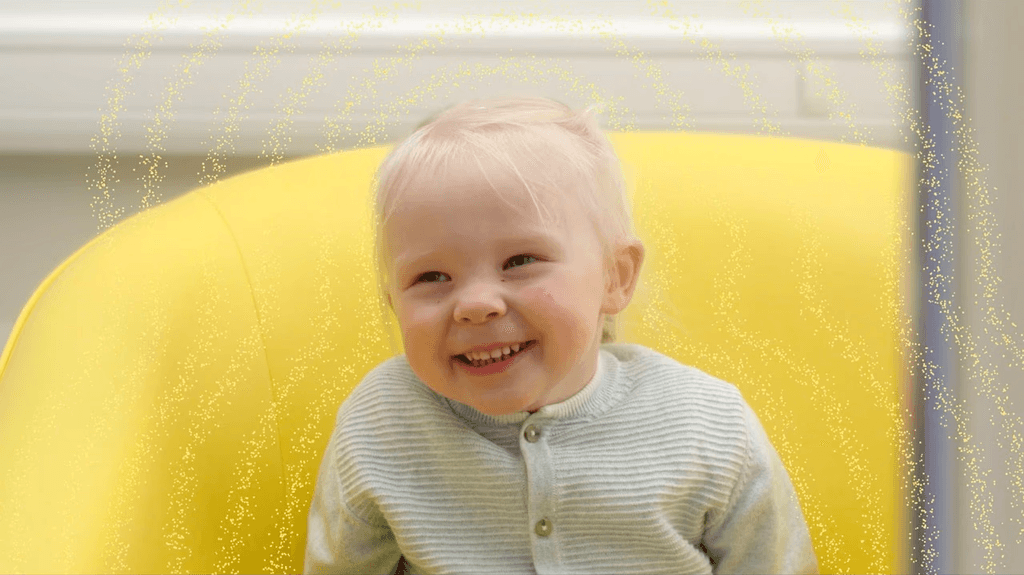 Screenshot from the ad, the little girl sits on a chair and smiles wide, with more sparkly lines emination from her (my animations).