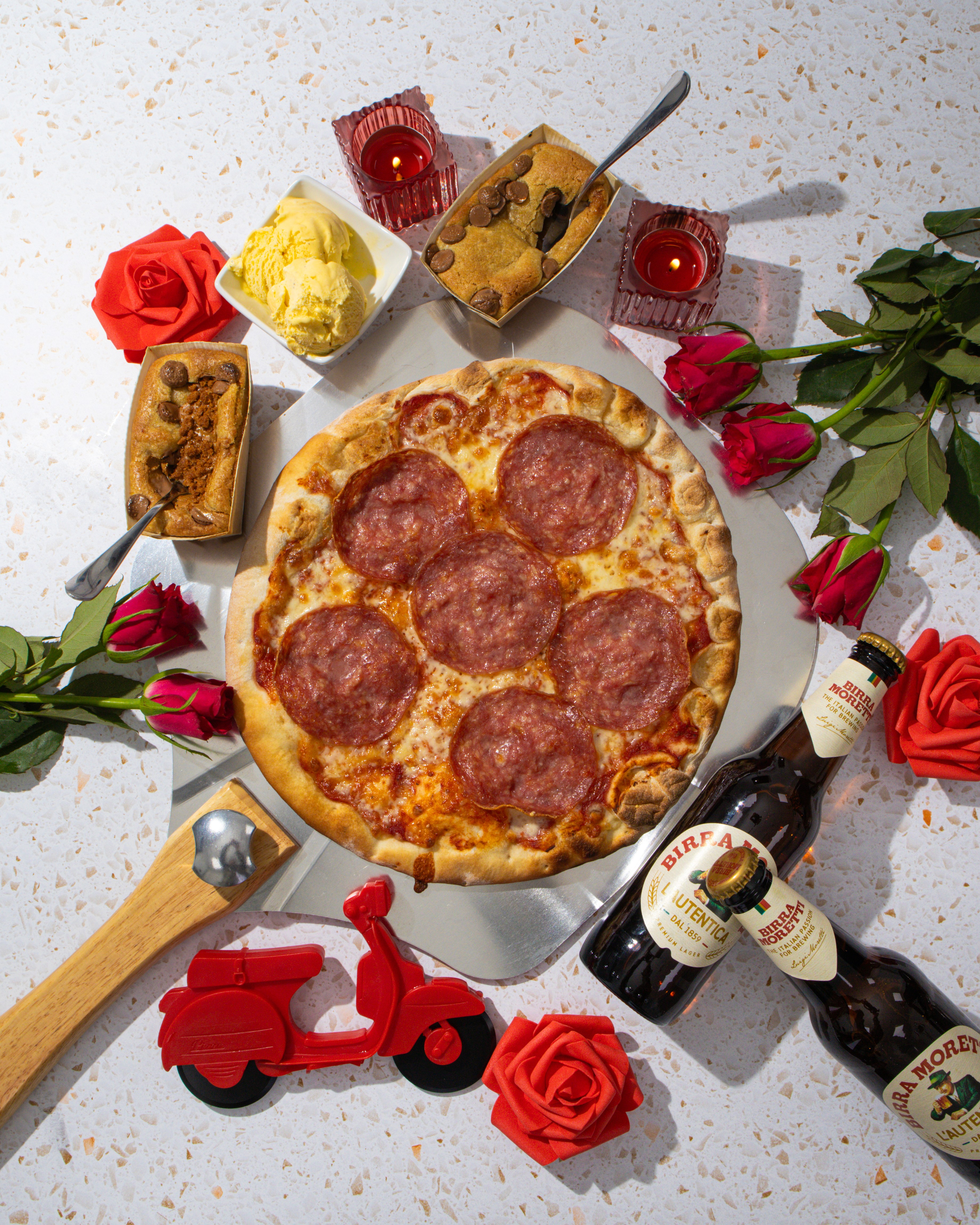Top down shot of a pizza, beer, and desserts