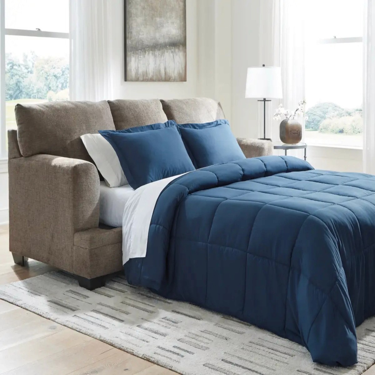 Brown sofa sleeper with blue bedding set, in a bright and airy bedroom