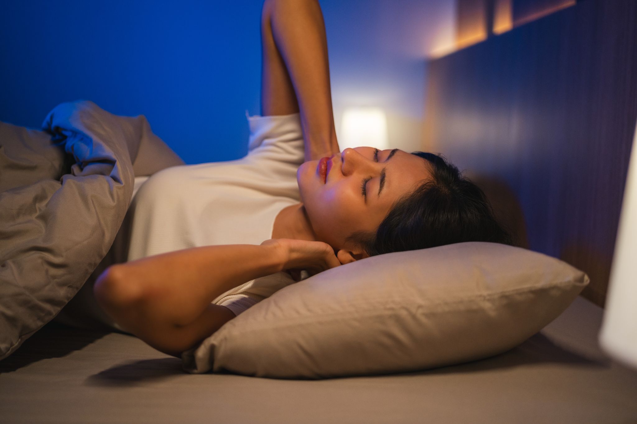 Woman touching her neck in bed at night, suffering from neck pain or stiffness.