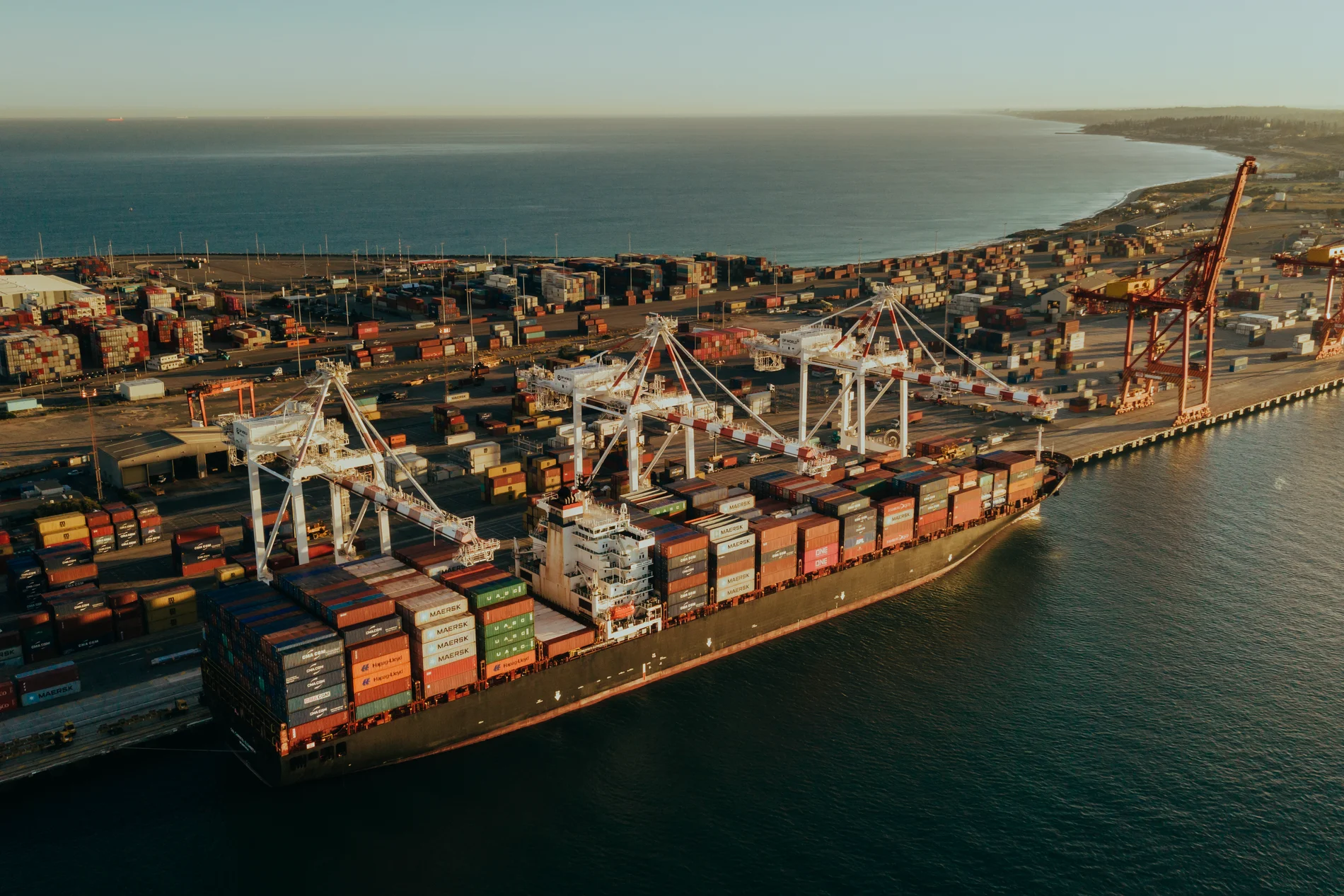 Aerial of a container ship alongside a terminal, cranes and yard stretching along the shore