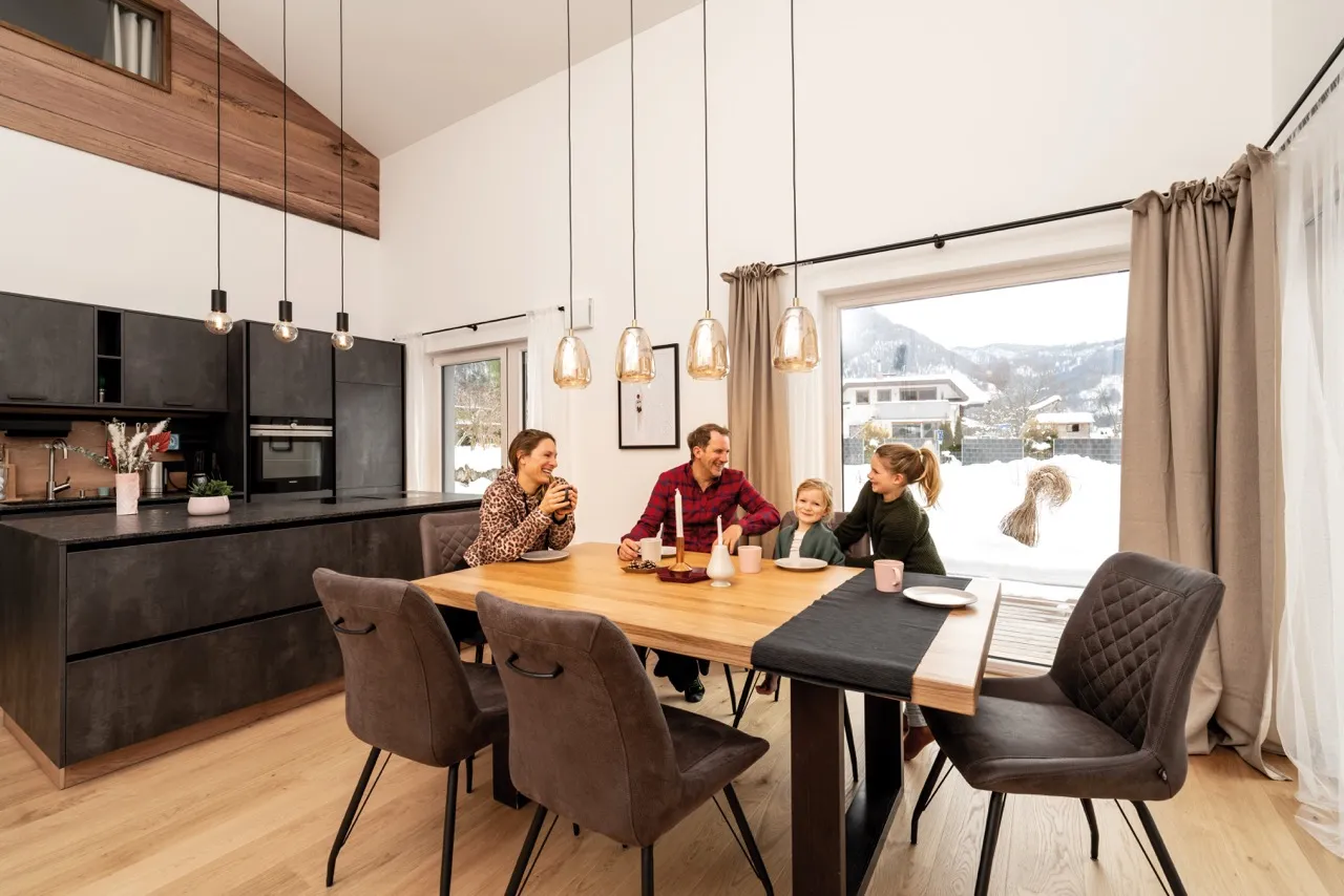 Glückliche Familie an einem Esstisch im modernen Esszimmer vor einem Fenster mit Schneelandschaft im Hintergrund.