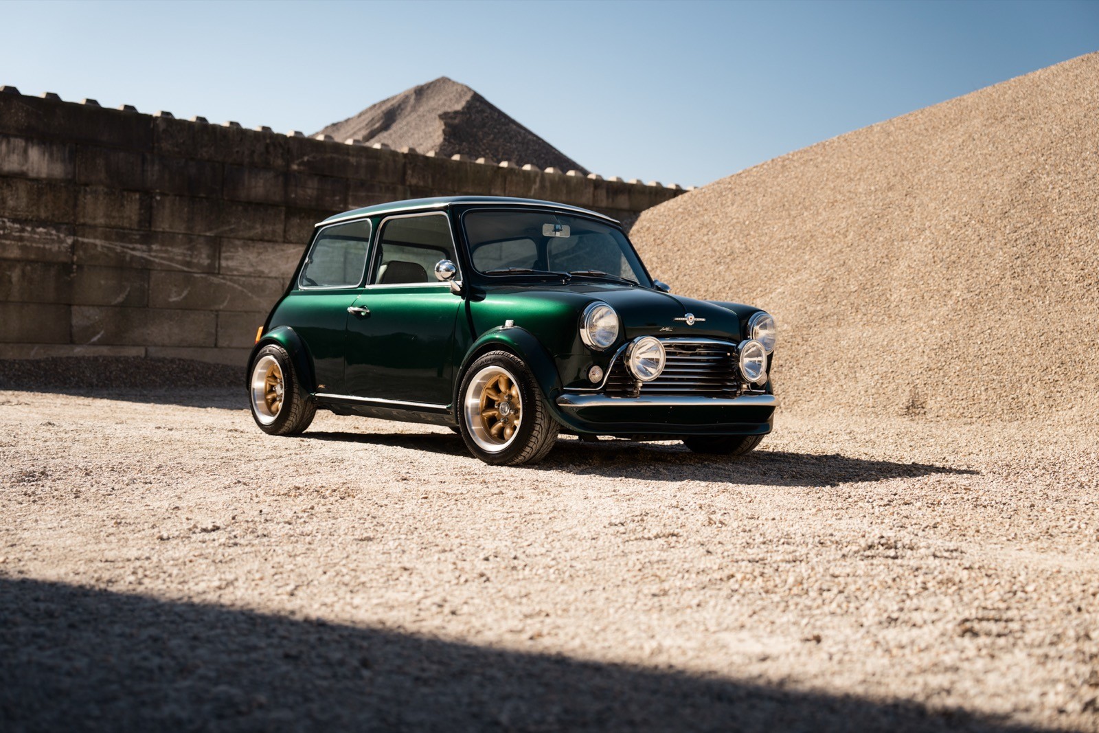 A small, green and black vehicle parked on a sandy surface, with a warm sunset lighting the scene.