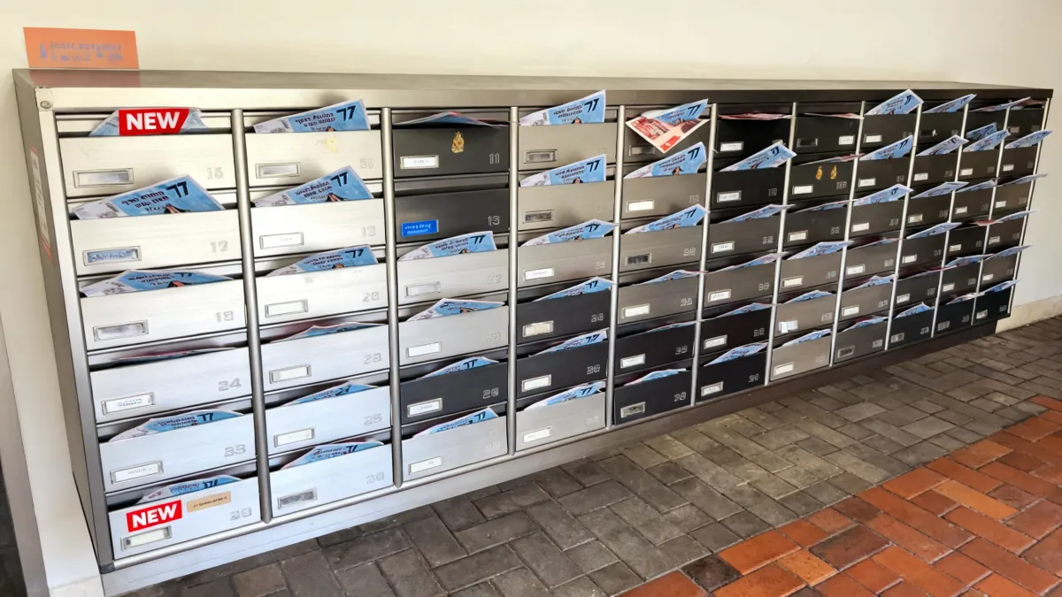 שורת תיבות דואר בבניין מגורים מלאות בפליירים של חברת עלונים, הממחישות הפצה רחבה ואפקטיבית של חומרי פרסום ישירות לפתח הבית של הלקוח.