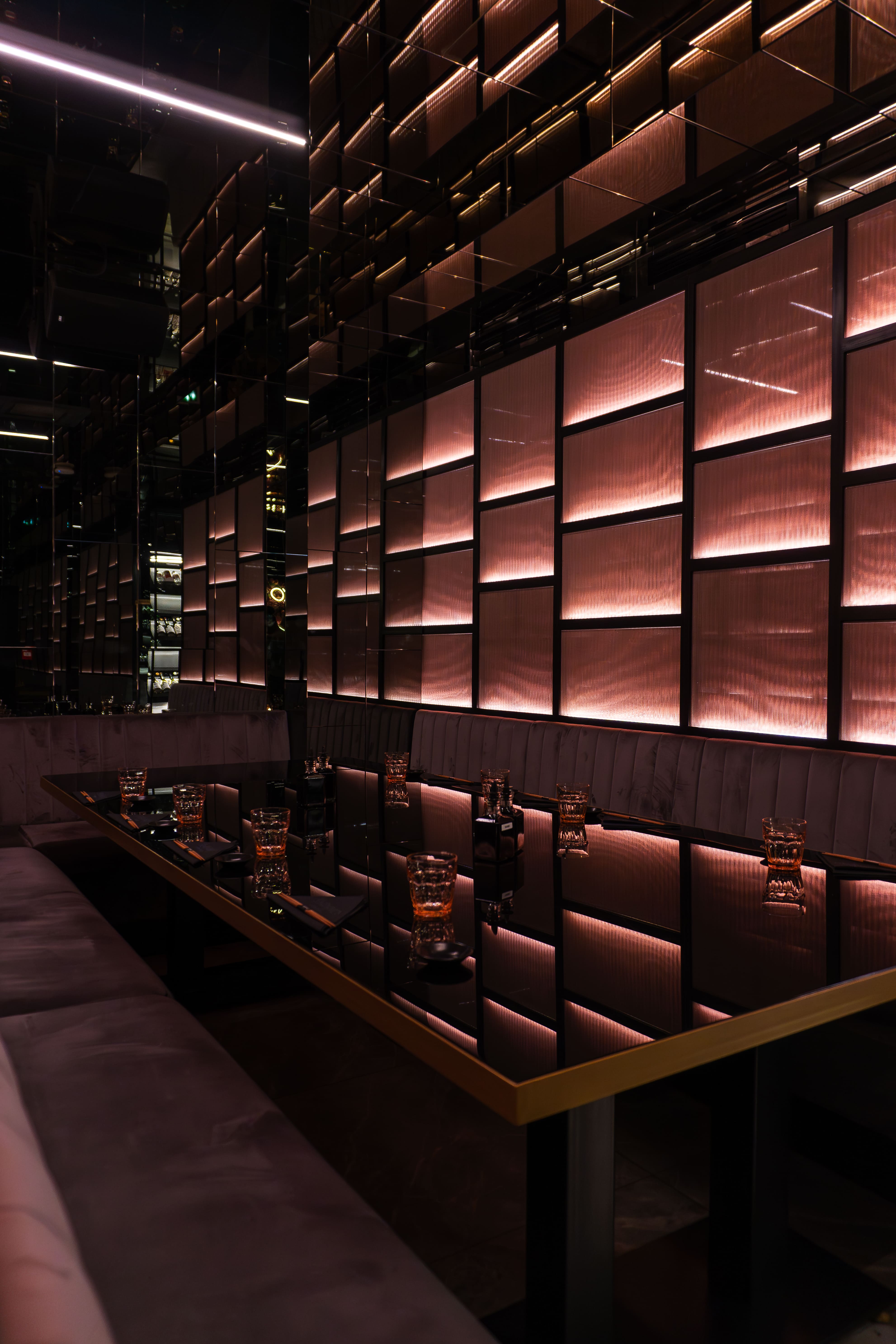 Elegant dining scene with a round table set for two, featuring a white tablecloth, three lit candles, and blue velvet chairs in a dimly-lit, plush setting.