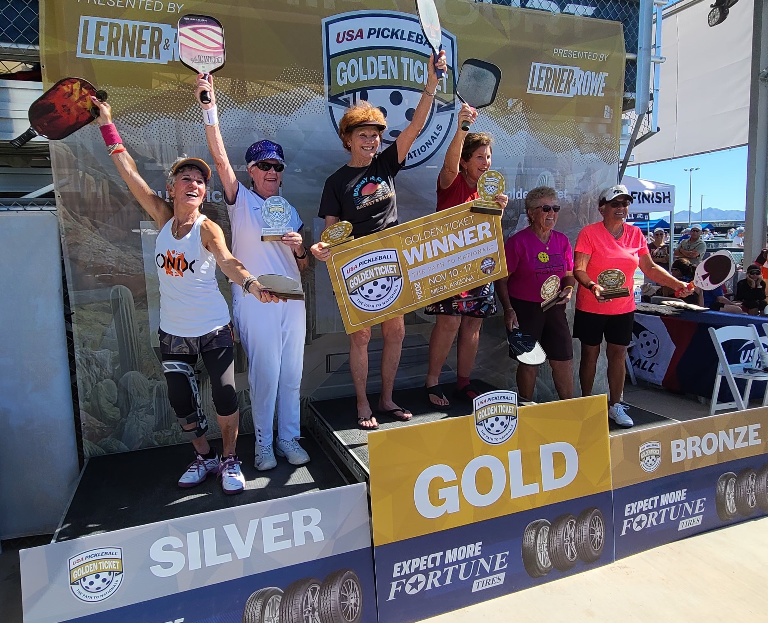 Pickleball players standing on a podium holding paddles and awards at a tournament event.
