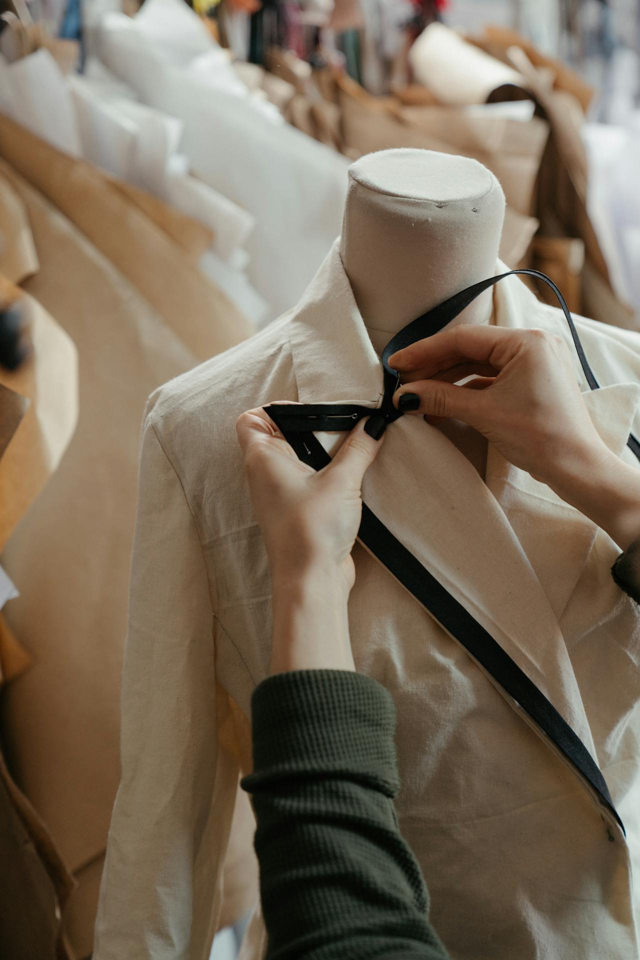 A person's hands adjusting a black ribbon on a white jacket on a mannequin