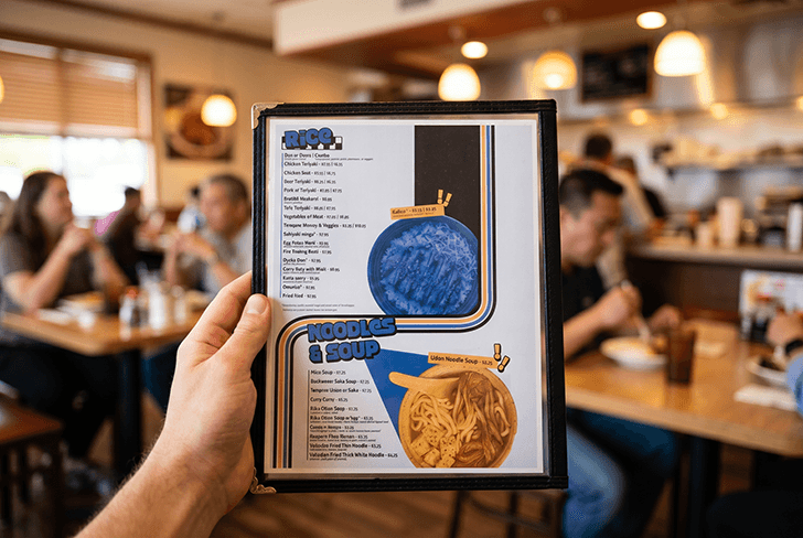 Back of menu is held up to camera in busy restaraunt.