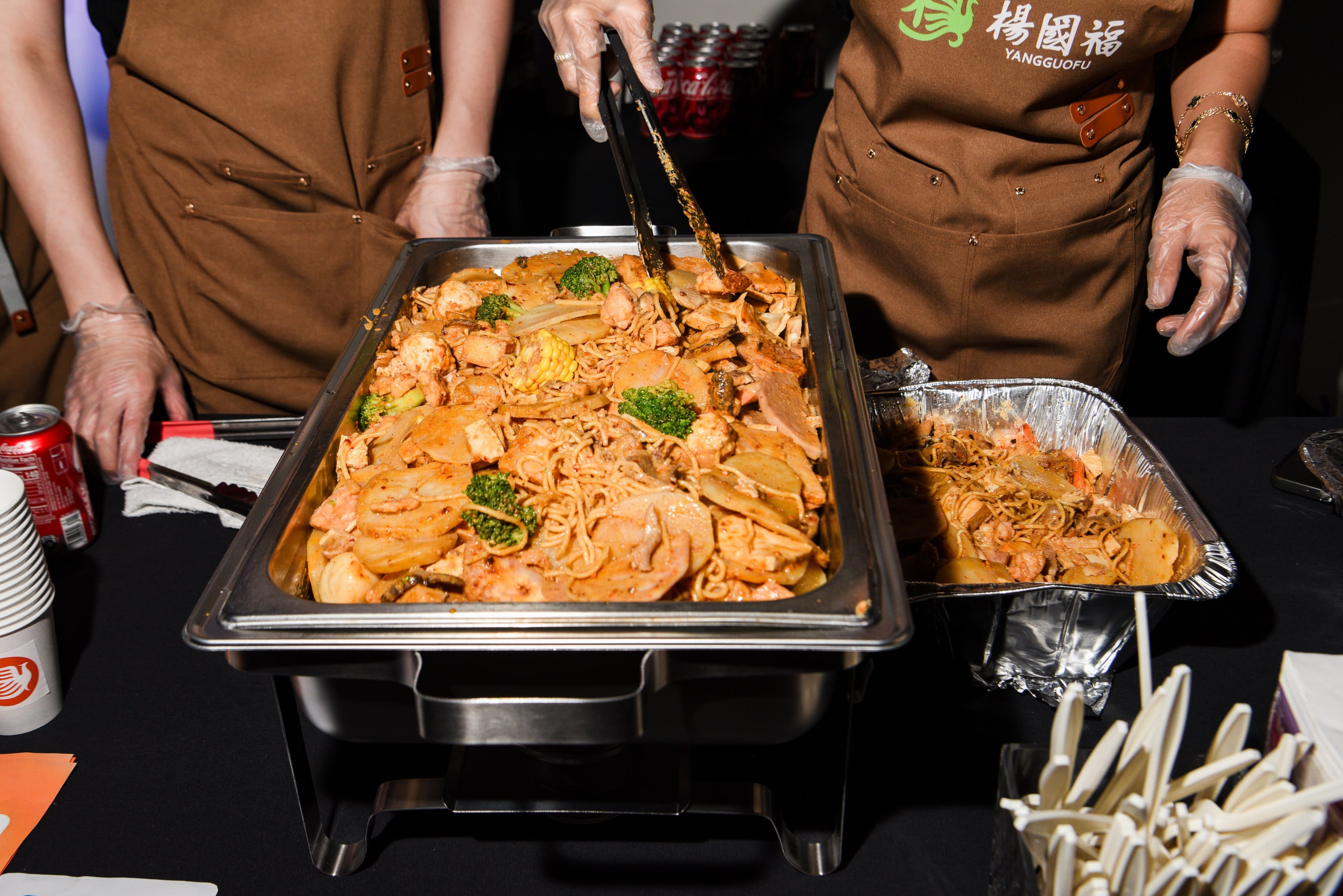 Stir fry with noodles, vegetables, and meat being served from a large warming dish.