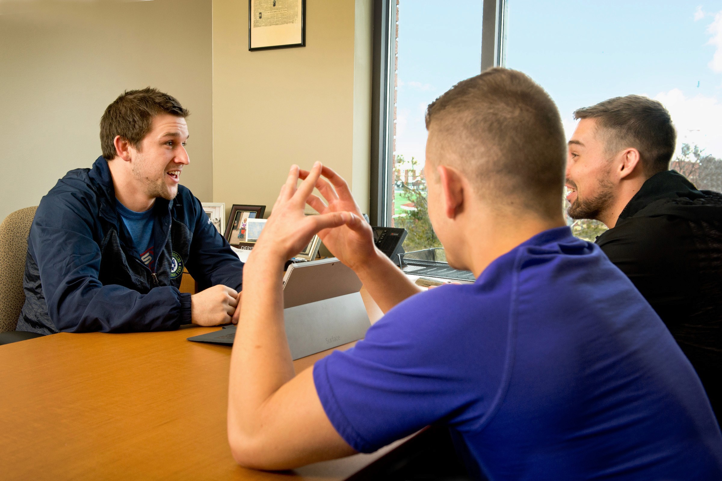 Coach sitting at a desk speaking with two athletes