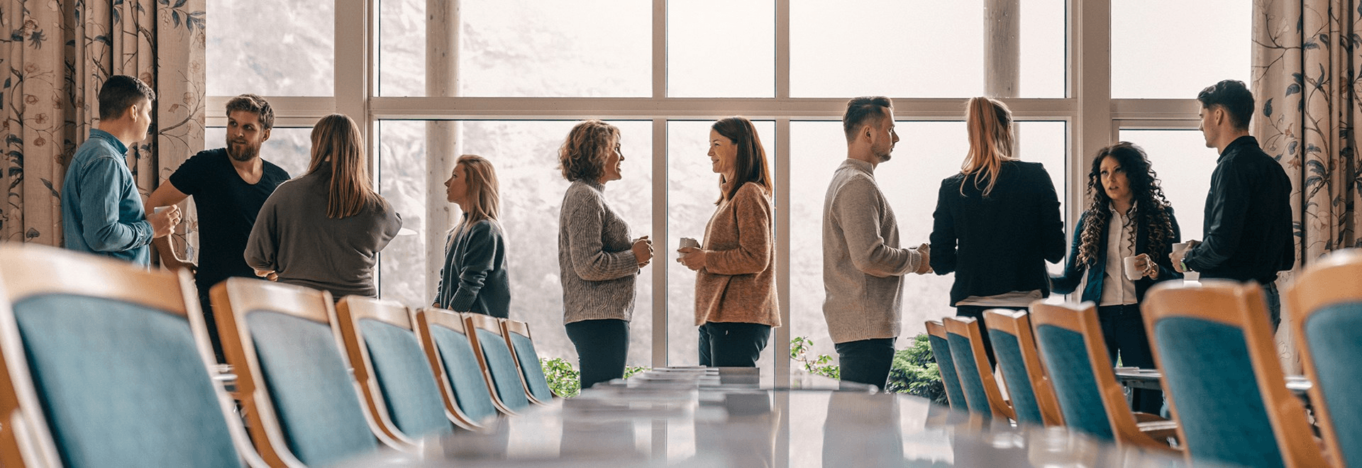 A group of people engaged in conversation, standing in a modern space with large windows.