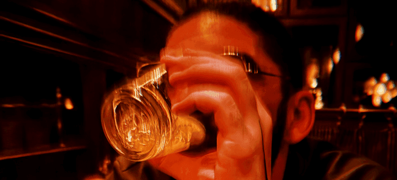 A close-up of a pink cocktail in a martini glass, set against a nighttime background with soft, blurred colors.
